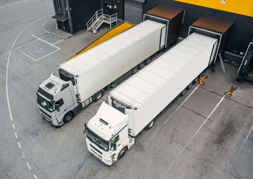 Two trucks pull out of a warehouse to illustrate that electric APUs last longer with lithium batteries